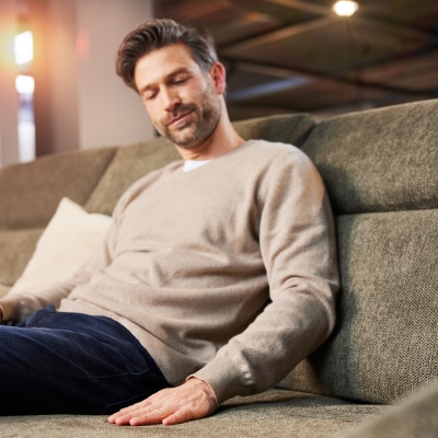 Ein Mann sitzt im Einrichtungshaus Möbel Weber und betrachtet fasziniert ein hochwertiges Interliving Sofa, beeindruckt von Design und Qualität.
