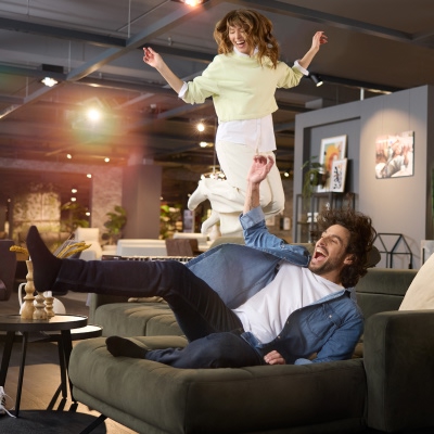 Ein glückliches Pärchen springt vor Freude auf seiner neuen Interliving Couch bei Möbel Weber – die perfekte Kombination aus Komfort und stilvollem Design.