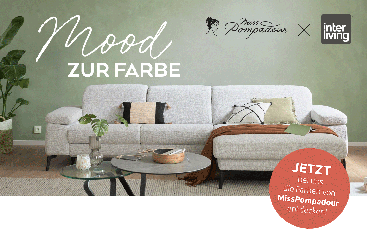 Korallfarbener Kreis mit „Jetzt bei uns die Farben von MissPompadour entdecken!“ auf einem stilvoll dekorierten grauen Sofa