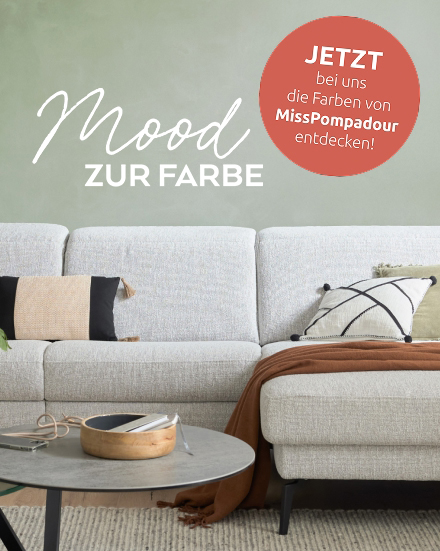 Korallfarbener Kreis mit „Jetzt bei uns die Farben von MissPompadour entdecken!“ auf einem stilvoll dekorierten grauen Sofa