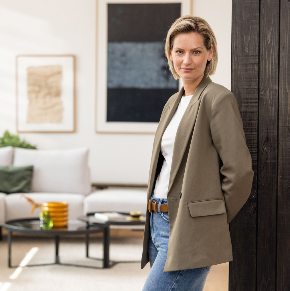 Blonde Frau in ihrem gemütlichen Wohnzimmer, umgeben von MissPompadour Wandfarben und stilvoller Einrichtung